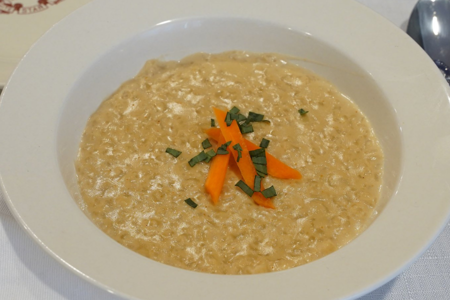Bowl of creamy oatmeal porridge topped with thin carrot strips and chopped herbs, representing Titanic’s third-class breakfast.