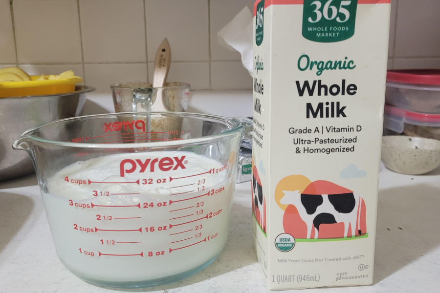 A carton of 365 Organic Whole Milk beside a Pyrex measuring cup filled with milk, with baking items in the background.