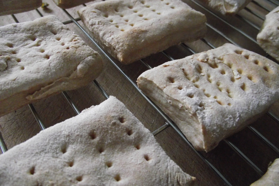 Homemade rectangular cabin biscuits cooling on a wire rack, lightly dusted with flour and marked with uniform pinholes.