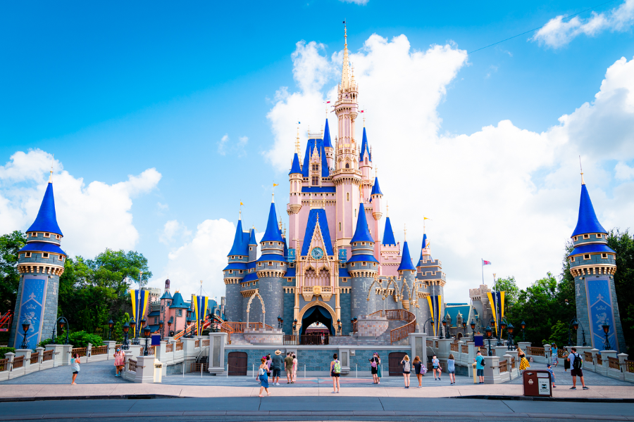 Visitors gather in front of Cinderella’s Castle at Walt Disney World, framed by bright blue skies and the castle’s iconic blue spires and golden accents.