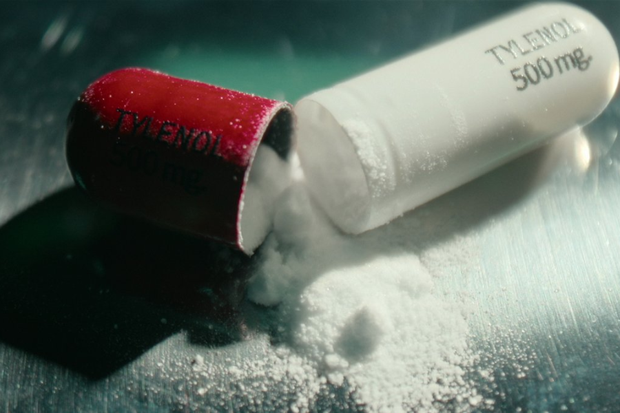 Close-up of a broken red and white Tylenol 500mg capsule with white powder spilling onto a reflective surface.