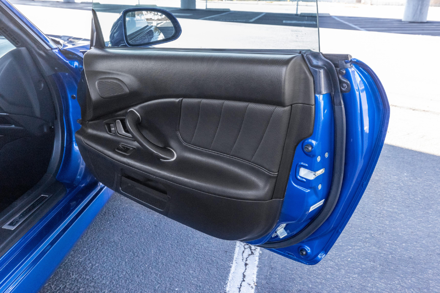 Open car door of a blue vehicle showcasing a black leather interior and visible locking mechanisms.