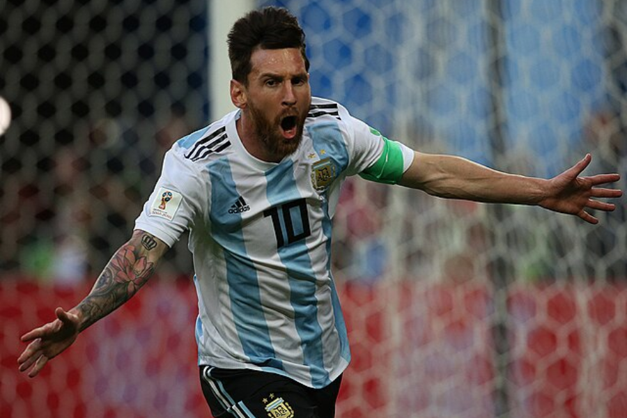 Soccer player in Argentina jersey with number 10 spreads arms wide in celebration on the field during a match.
