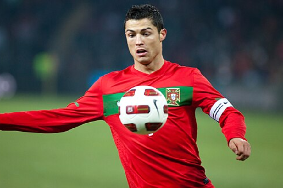 Soccer player in a red Portugal jersey and captain's armband controls a soccer ball mid-game.
