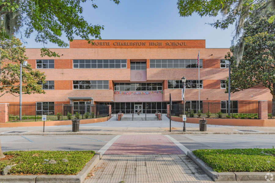  Exterior view of North Charleston High School, a large brick building with black gates and American flags.