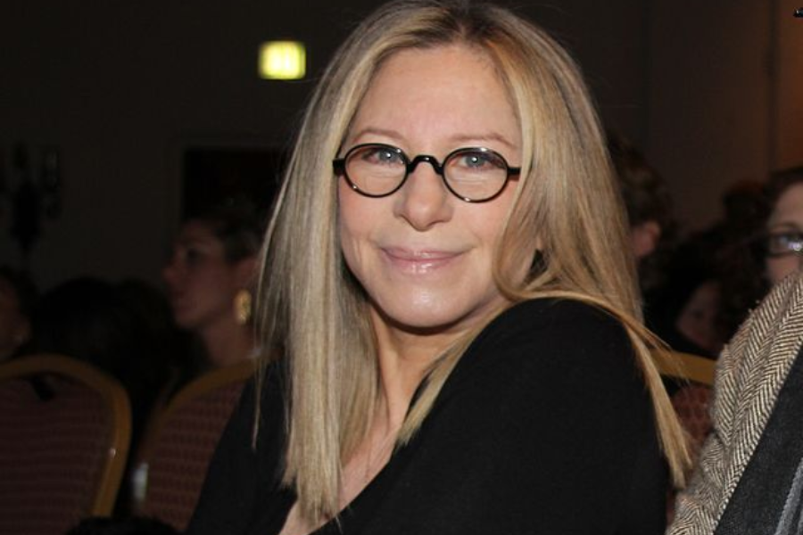 Woman with straight blonde hair and round glasses smiles while seated at an indoor event.