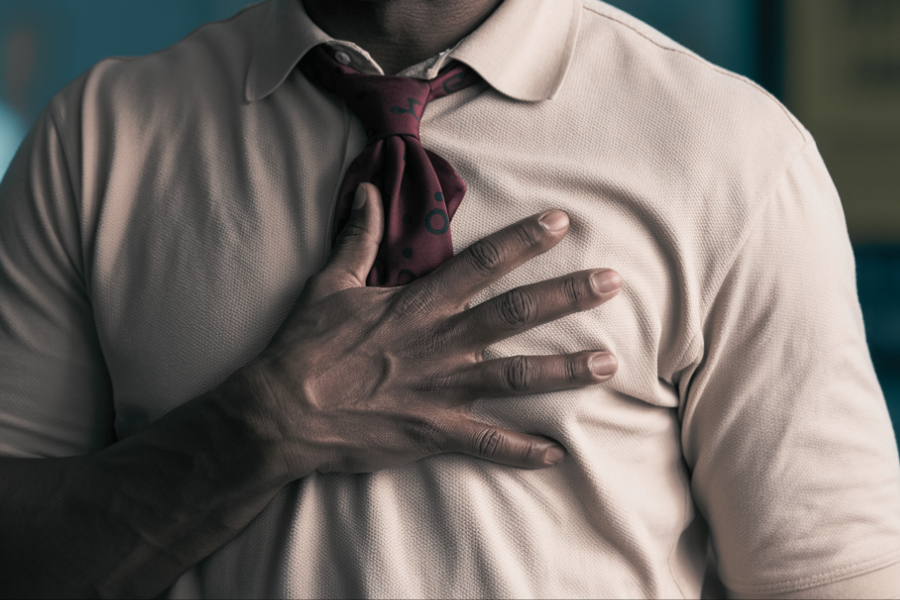 A man wearing a cream polo shirt and red tie places a hand over his heart in a gesture that could suggest sincerity, emotion, or a pledge.
