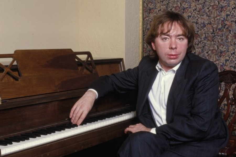 Man in a pinstripe suit sits at an upright piano with one hand resting on the keys in a formal portrait.