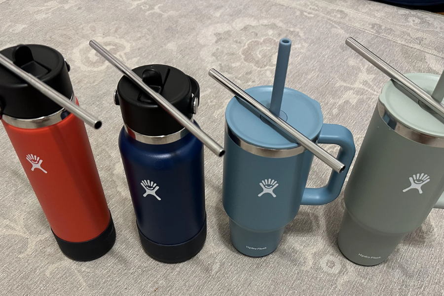 Four colorful Hydro Flask containers with stainless steel straws laid across the tops, sitting on a patterned rug.