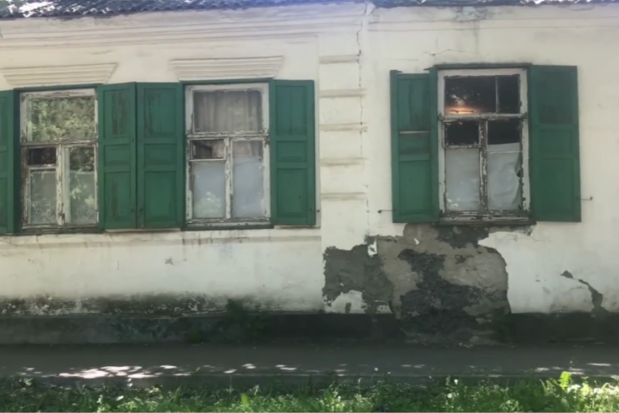 Weathered white building with peeling paint and green wooden shutters on its old windows.