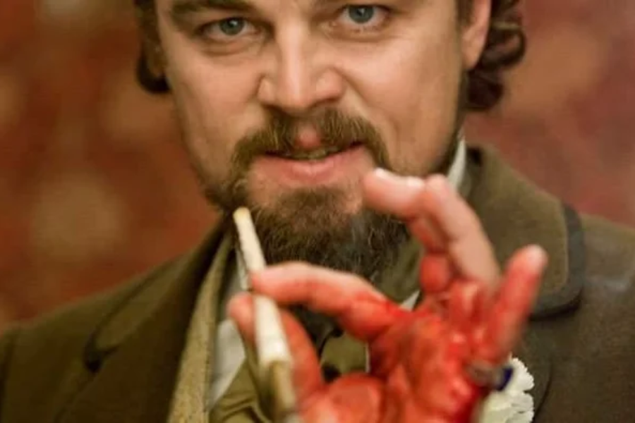 A man with a bloody hand holds a cigarette and smirks menacingly while staring intensely at the camera.