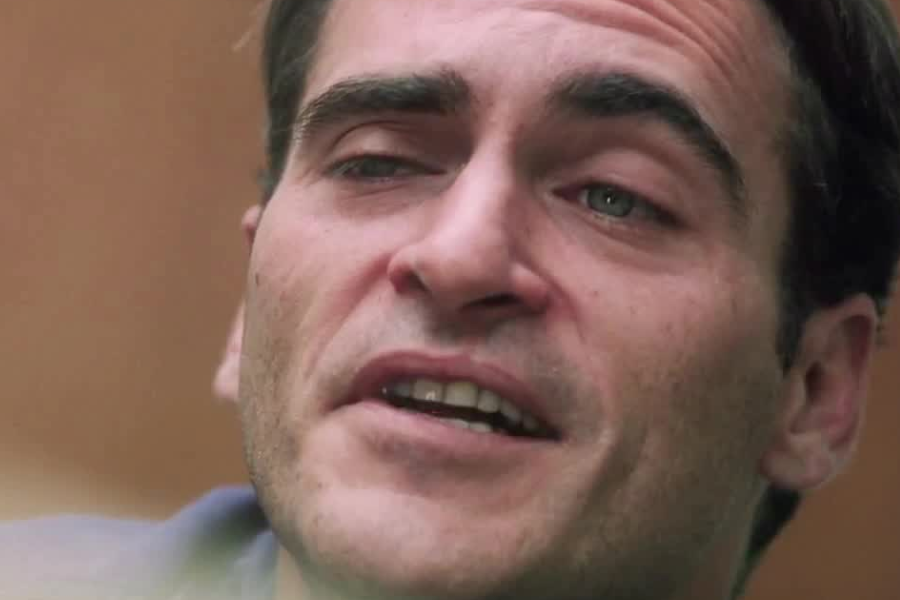 A close-up of a man with slicked hair and a pained, emotional expression as he looks slightly upward.
