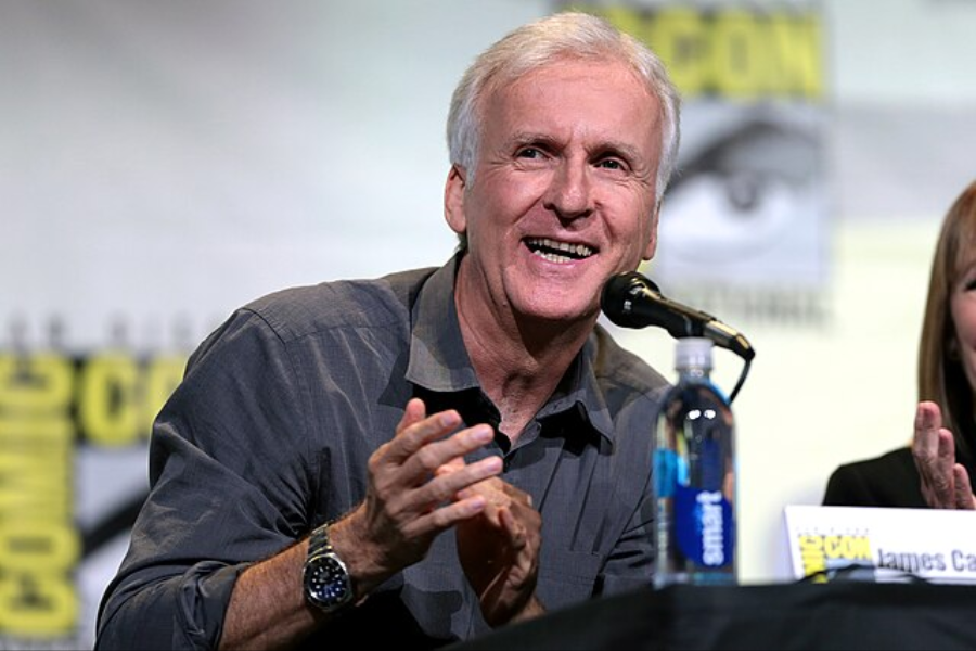 Smiling man speaks into a microphone during a panel event, gesturing with his hands while seated next to others.