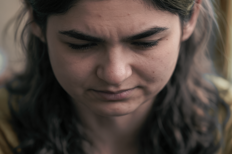 A close-up of a young girl’s face looking downward with a furrowed brow, suggesting she is deep in thought or emotionally overwhelmed.