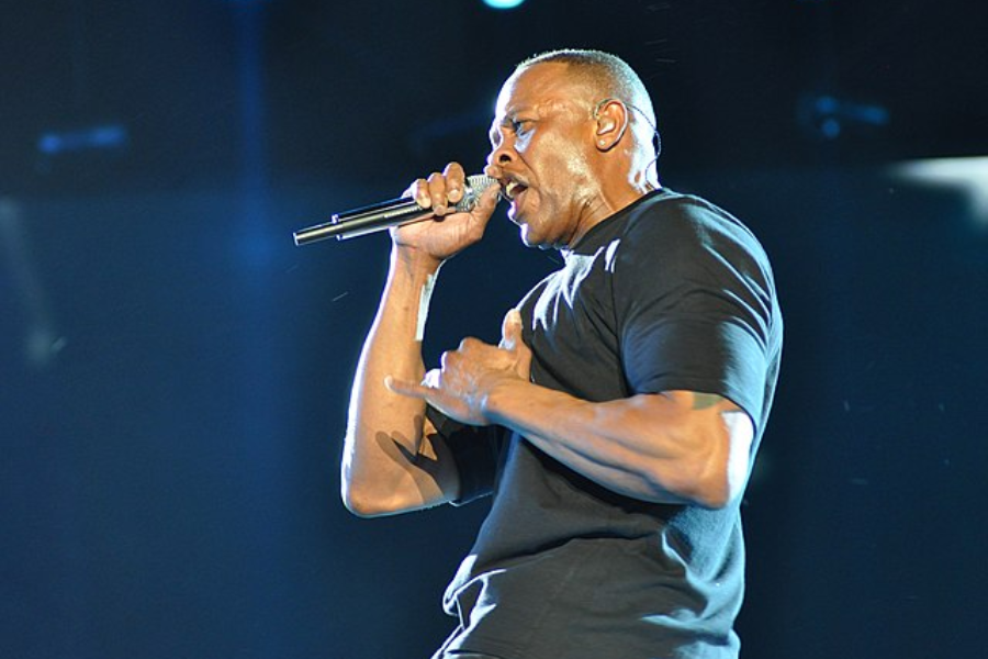 Man in a black t-shirt performs on stage with intense expression, holding a microphone mid-rap.