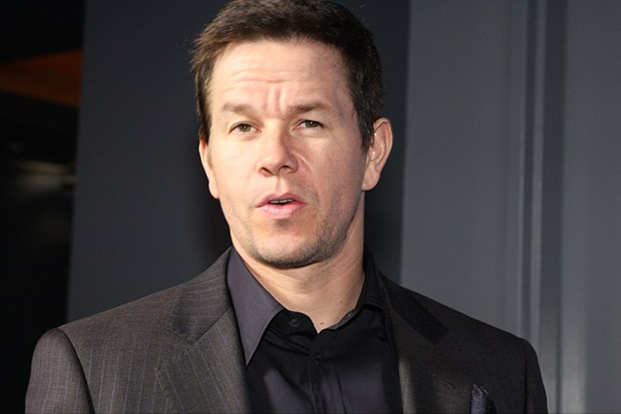 Man in a dark suit with a slightly raised eyebrow poses for a photo against a dark background.