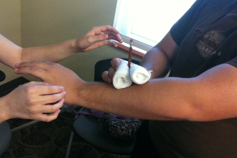 Arm splint being applied using rolled gauze and a pencil as a makeshift stabilizer during a first aid demonstration.