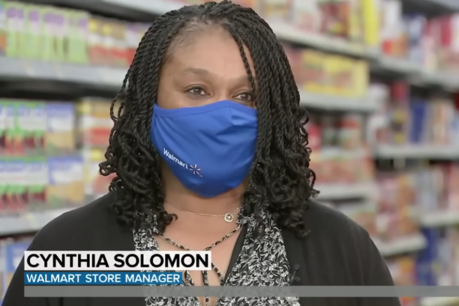 Walmart store manager Cynthia Solomon wears a blue branded mask while speaking in a grocery aisle.