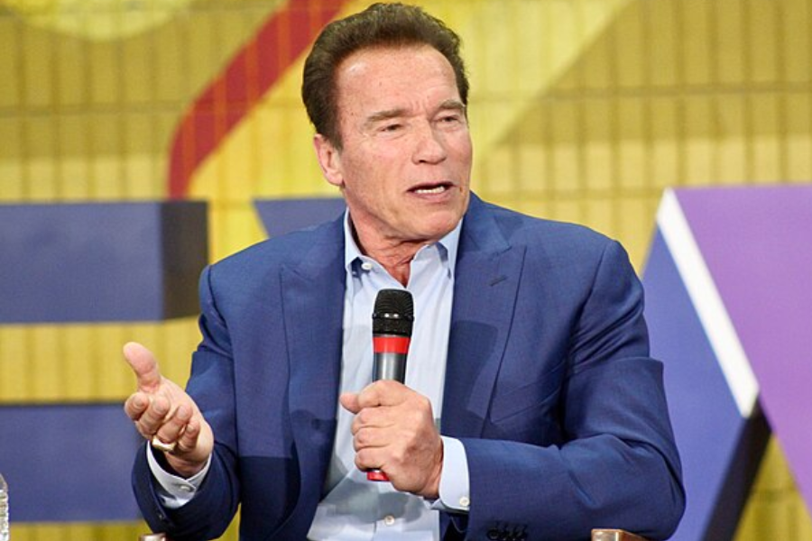 Man in a blue blazer gestures with one hand while speaking into a microphone during a panel discussion.