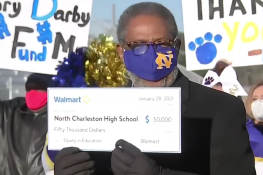 Henry Darby holds an oversized $50,000 Walmart check for North Charleston High School while standing in front of cheering supporters.