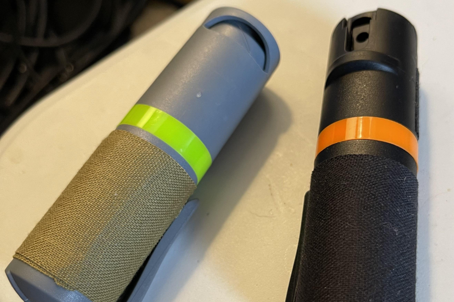 Two canisters of bear spray with safety caps and fabric grips, lying on a white surface.
