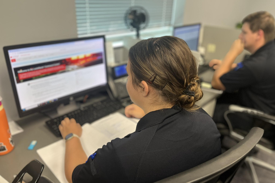 Two people in uniform sitting at computers, with one focused on a screen displaying emergency management content.