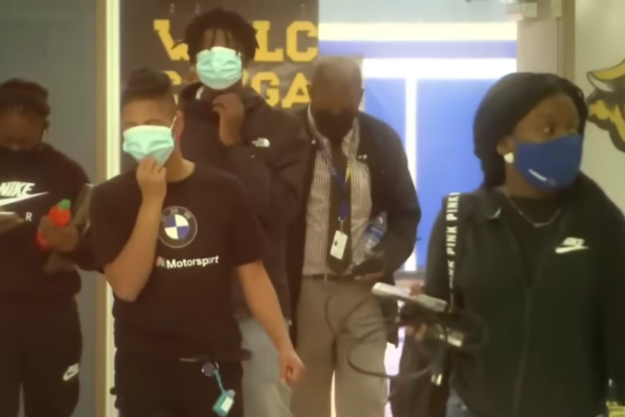 Group of masked students walk through a school hallway with Henry Darby following behind.