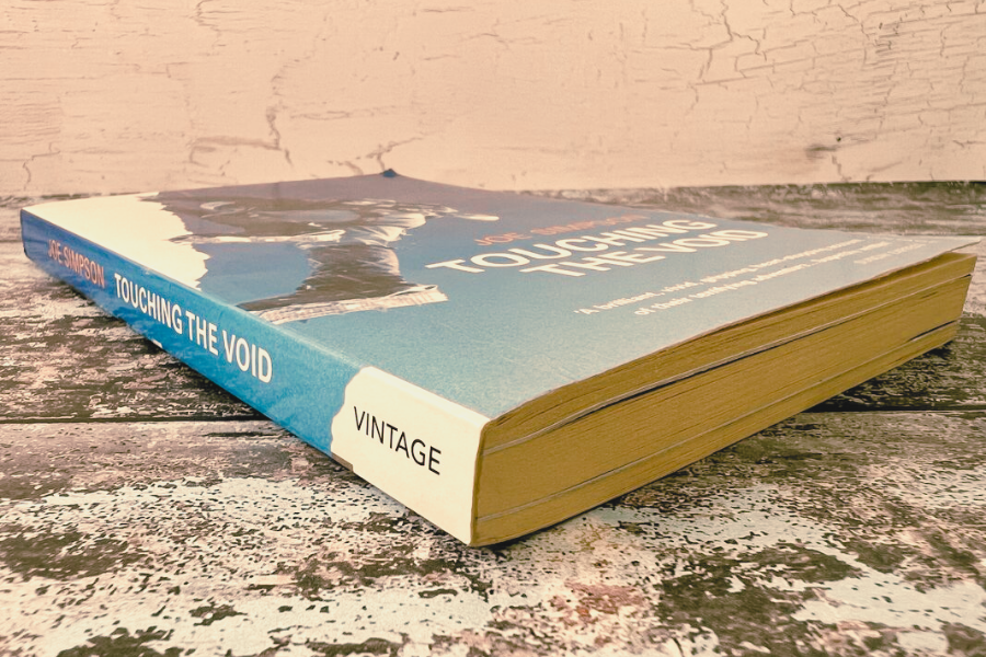 The book Touching the Void by Joe Simpson lies on a weathered wooden surface, its spine showing the title and publisher Vintage.