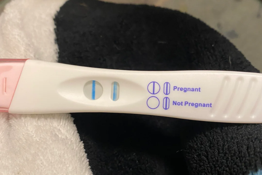 Positive pregnancy test with two blue lines resting on a black and white towel.