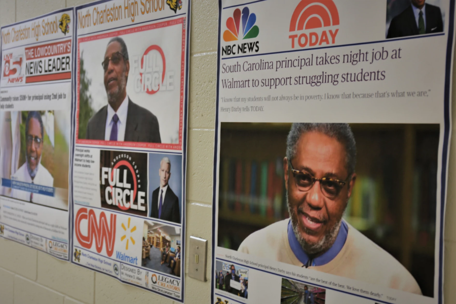 Posters on a school wall display national news coverage of Henry Darby taking a Walmart night job to support students.