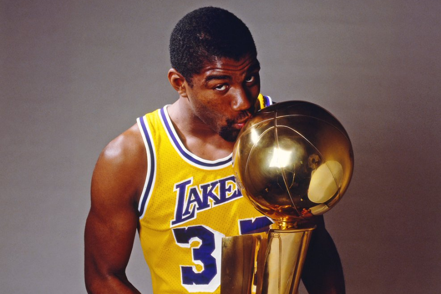 Man in a yellow Lakers jersey kisses a shiny gold NBA championship trophy while posing for a portrait.