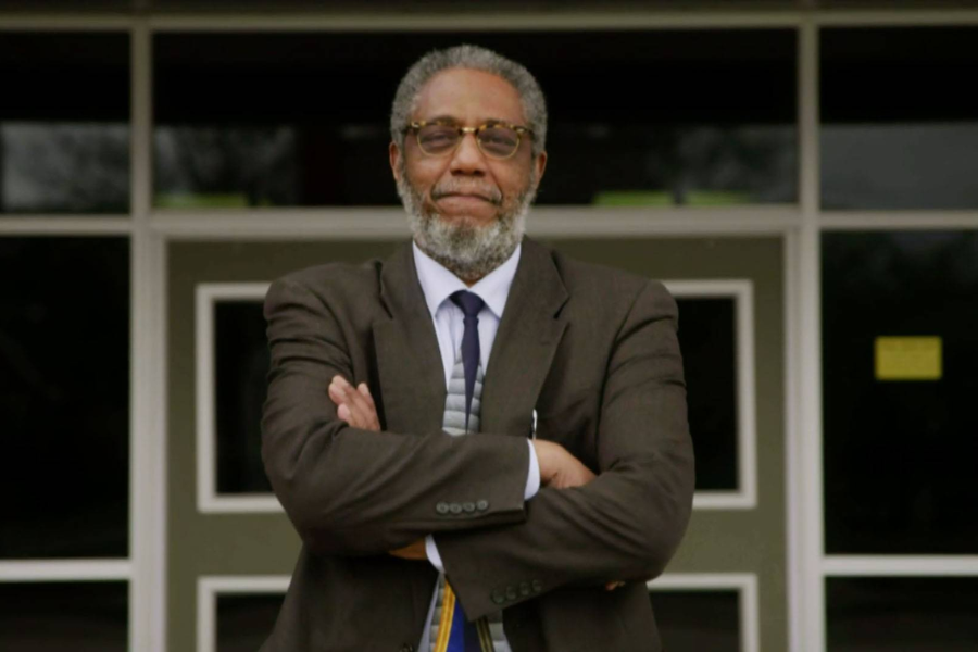 Henry Darby stands confidently with arms crossed in front of school entrance doors.