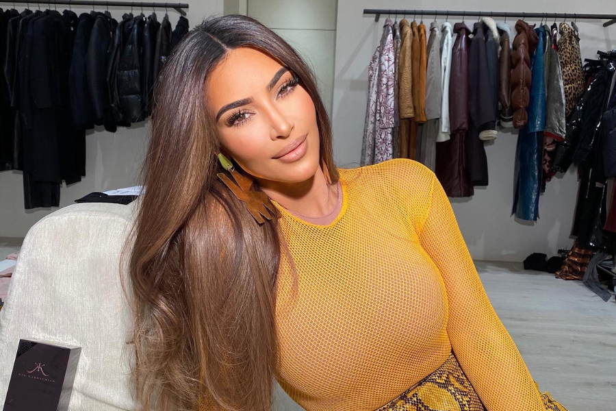 Woman in a fitted yellow mesh top poses confidently in a boutique space with clothing racks behind her.
