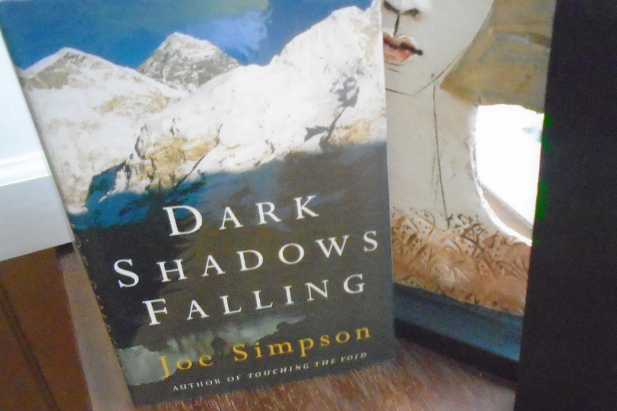 paperback copy of Dark Shadows Falling by Joe Simpson stands upright on a shelf, showing snow-covered peaks and the subtitle "Author of Touching the Void".
