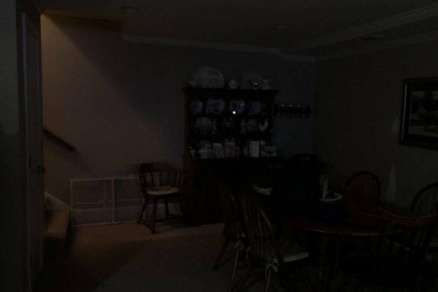 Dimly lit dining room with a staircase, wooden furniture, and decorative china cabinet barely visible in low light.