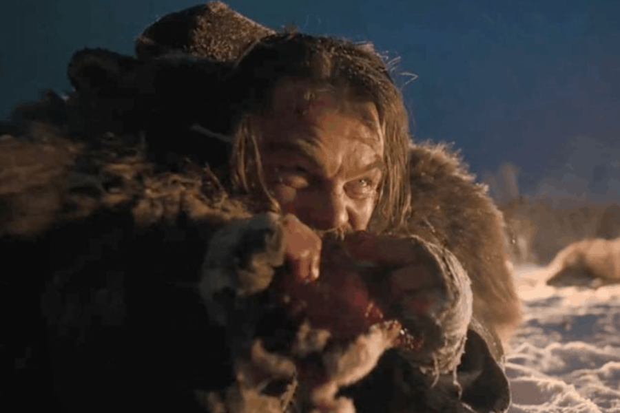 A fur-clad man kneels in the snow at night, aggressively biting into raw meat with visible desperation.
