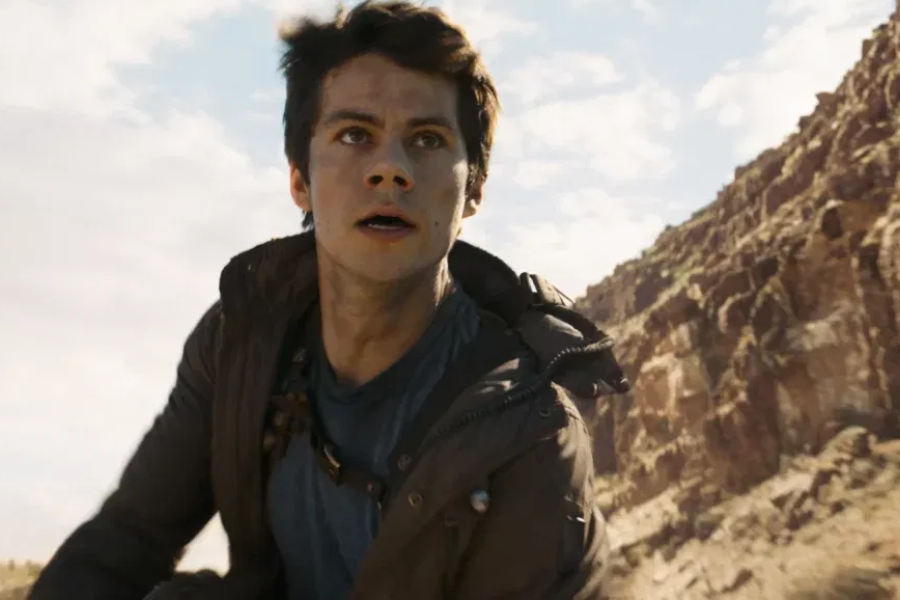 A young man in a dark jacket looks up anxiously while standing in a rocky desert landscape.