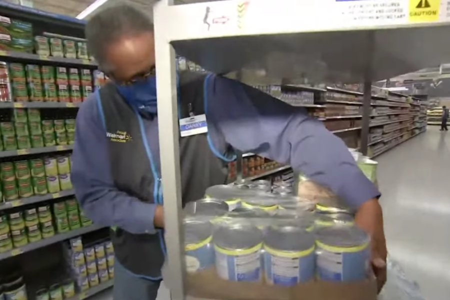 Walmart worker arranges a tray of canned goods on a shelf from a stocking cart in the canned vegetable aisle.