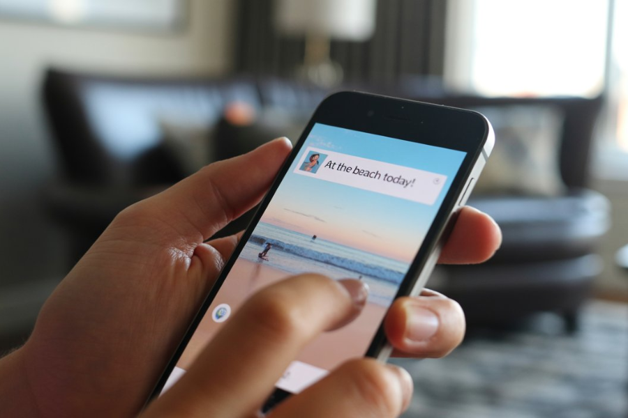 Hand holding a smartphone with a social media post displaying a beach photo and the caption “At the beach today!”.