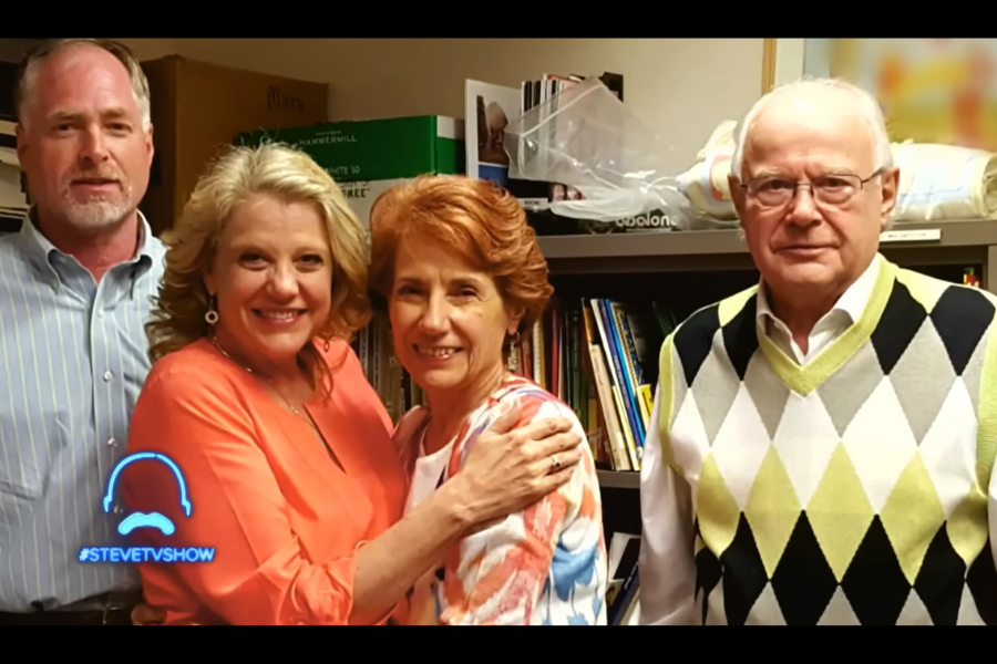 Four adults stand together smiling in a library setting, with bookshelves behind them.