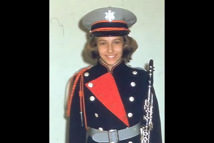 Color photo of a young woman in a marching band uniform holding a clarinet, smiling at the camera.