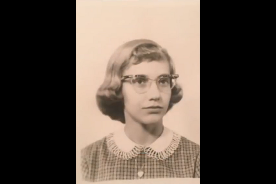 A vintage sepia toned school portrait of a young girl in glasses and a checkered dress with a lace collar.