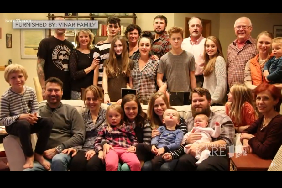 Large extended family group photo taken indoors, with multiple adults and children sitting and standing together, smiling at the camera.
