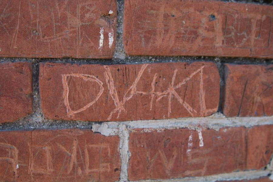 Close up of a red brick wall with letters scratched into the surface reading DV+KL. The carving sits on a single brick.