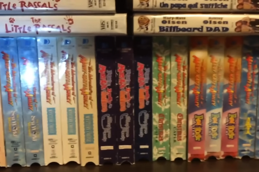 A VHS shelf featuring multiple Mary-Kate and Ashley Olsen films, including "Billboard Dad," "You're Invited," and "The Adventures of Mary-Kate & Ashley." The tapes are neatly organized by title and series.