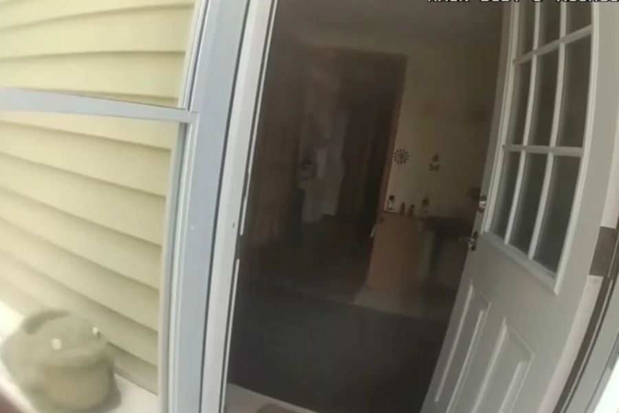 View from a body camera showing an open front door leading into a dimly lit home interior.