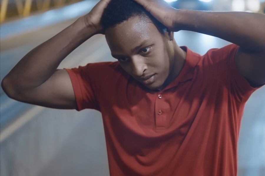 A concerned young man in a red shirt holding his hands behind his head under street lights at night.