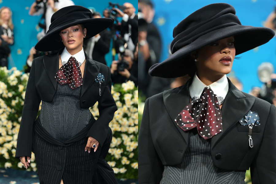 Woman wearing a dramatic oversized black hat and structured pinstripe gown with a cropped jacket, accessorized with layered polka-dot neckties and brooch. Close-up captures her bold lip and confident gaze.