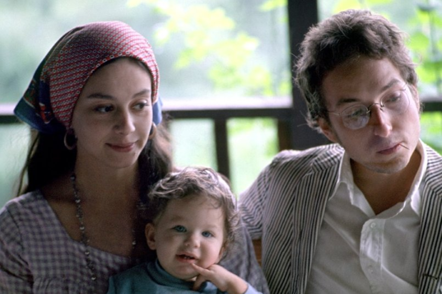 Color photo of Bob Dylan with Sara Dylan and their young child, sitting together on a porch with a calm, intimate vibe.