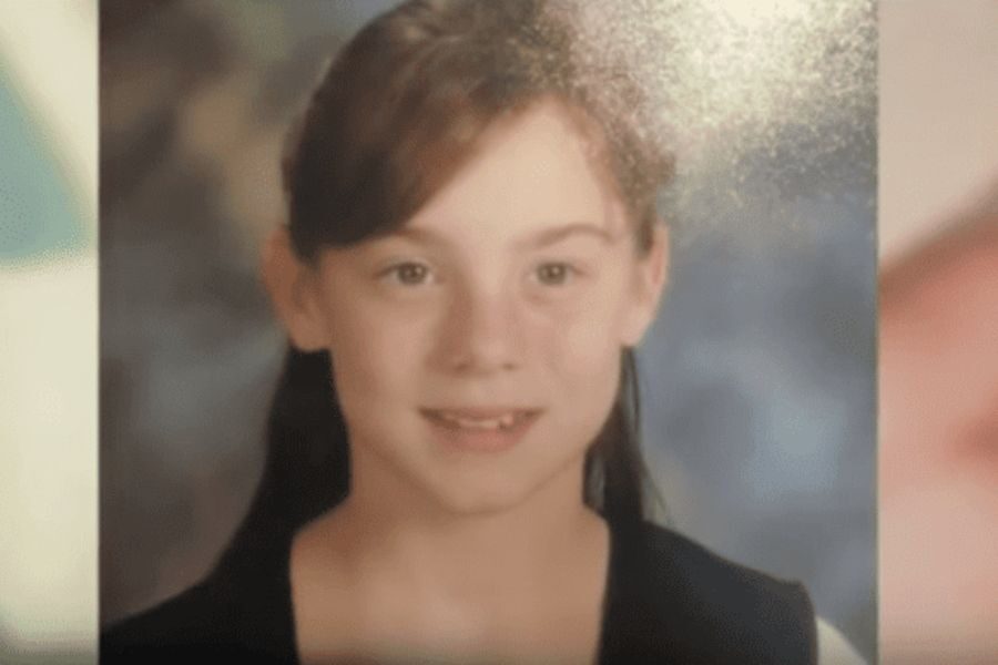 School portrait of a young girl with a neutral expression, light skin, and dark hair pulled back, wearing a dark vest over a white shirt.